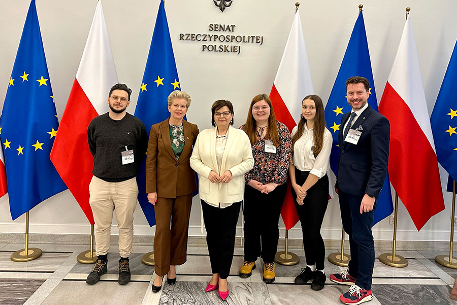 Grupa osób, studentów i opiekuna z WUM oraz minister zdrowia i przewodniczącej komisji. Stoją i uśmiechają się do aparatu. Za nimi flagi - Polski i UE